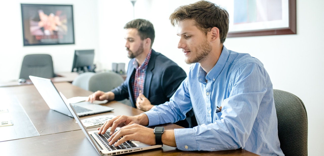 Two men working on laptops in a boardroom setting