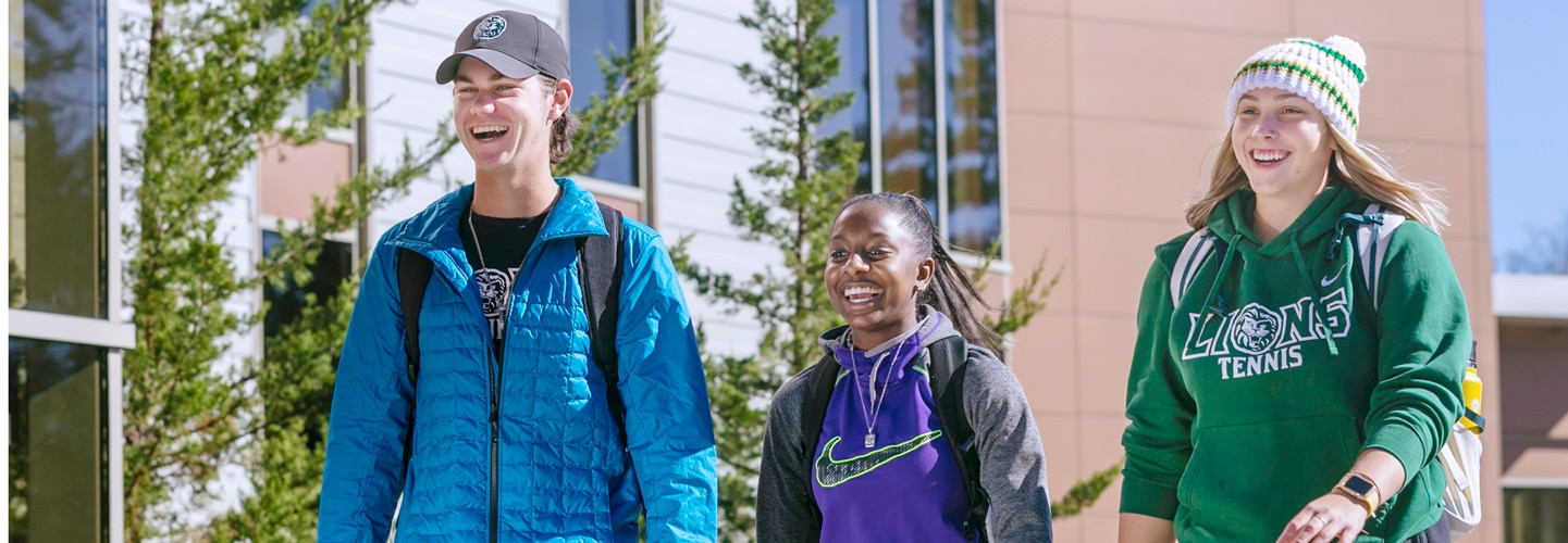 Three students smiling and walking through campus