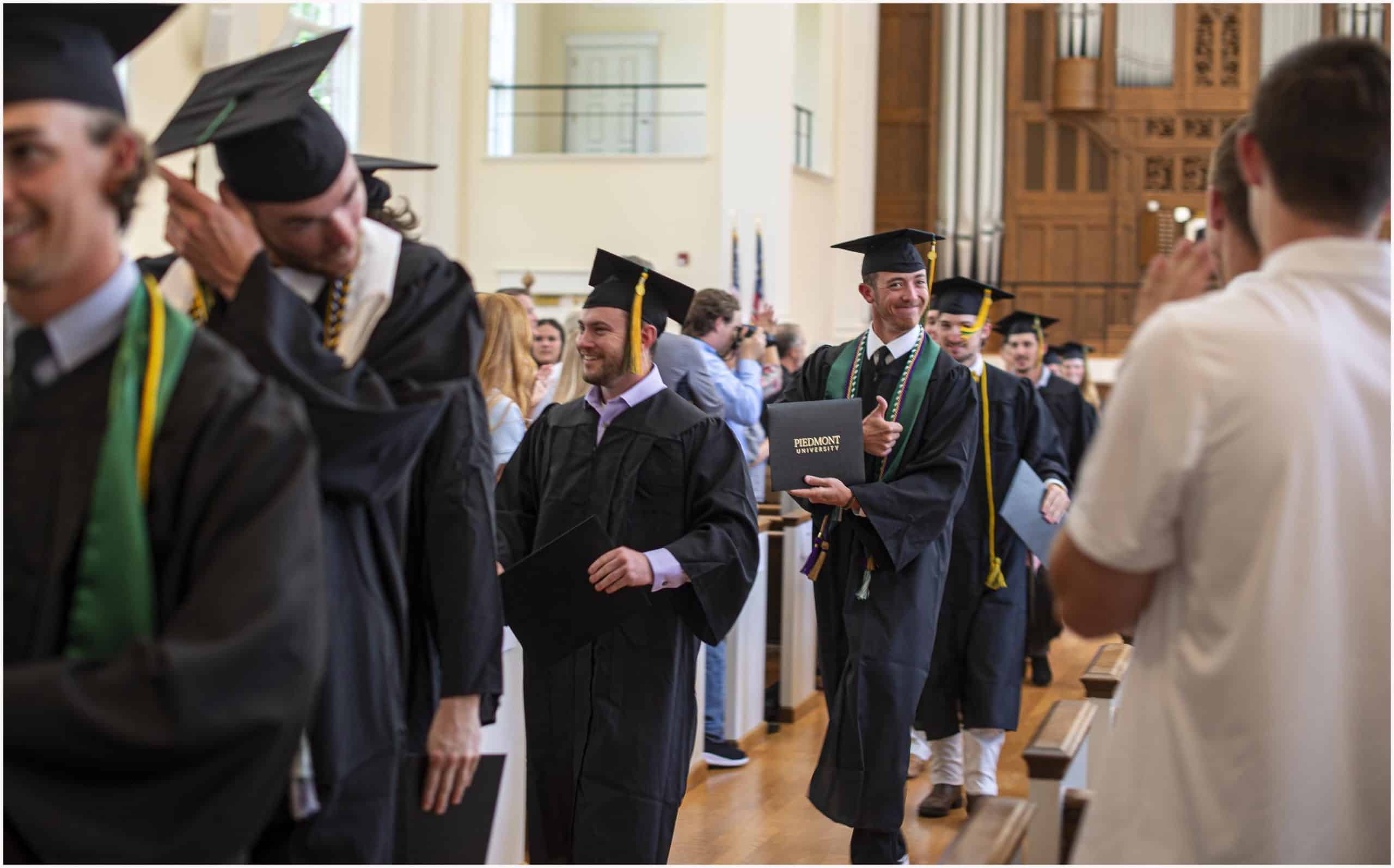 Line of graduates that have received their diplomas walking down an aisle