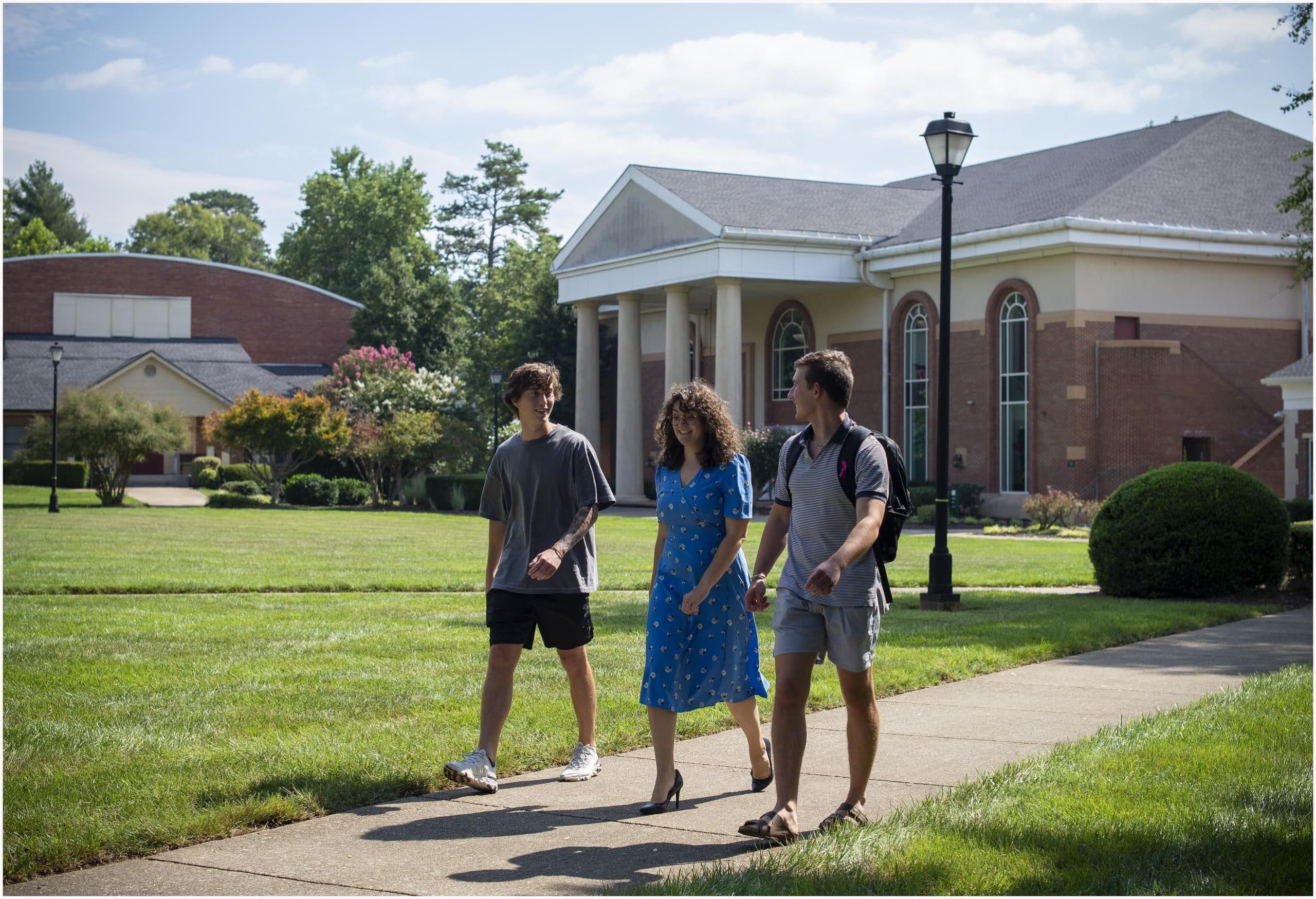 Two men and one woman walking along a sidewalk on campus