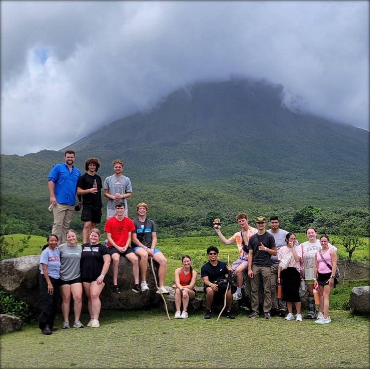 Students sitting at the base of a mountain with dense cloud cover